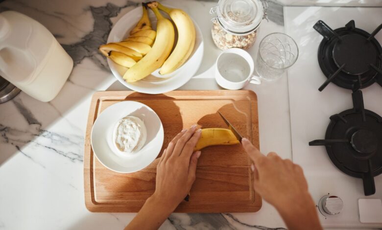 Person slicing banana on wooden board with cereals and milk for a healthy breakfast.