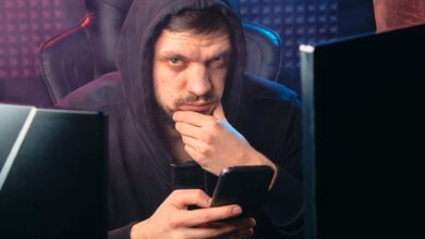 A man in a black hoodie contemplating while using a smartphone, surrounded by digital screens.