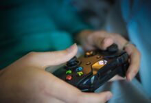 Hands gripping a modern wireless gaming controller indoors. Perfect for tech enthusiasts.