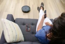 Person relaxing on a sofa controlling a robot vacuum cleaner with a remote.