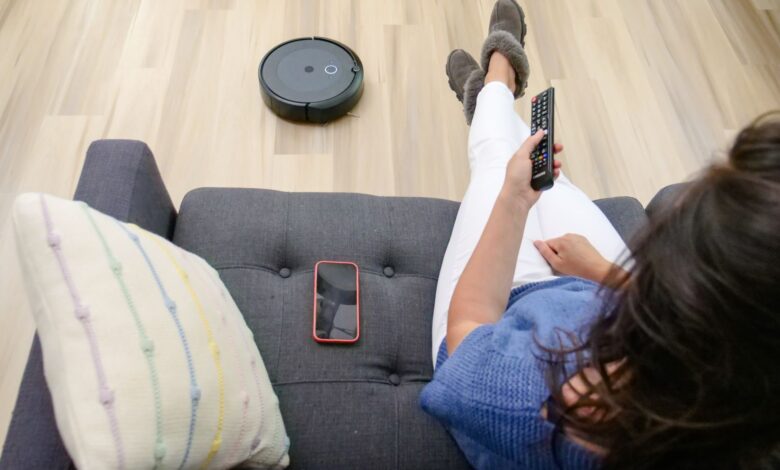 Person relaxing on a sofa controlling a robot vacuum cleaner with a remote.