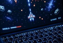 A classic arcade space shooter game displayed on a laptop with illuminated keyboard, showing retro graphics.