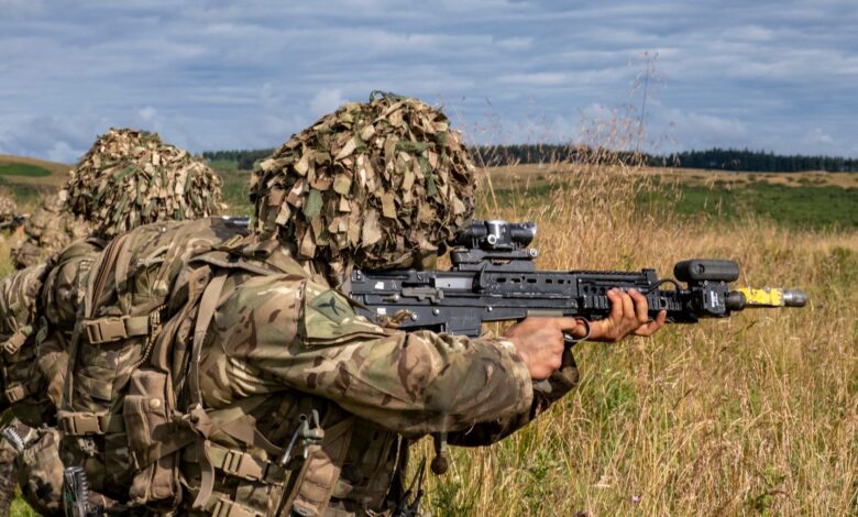 Military soldiers in camouflage gear practicing combat in a grassy countryside.