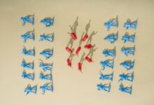 Blue and red toy soldiers arranged on a yellow background with artistic shadows.