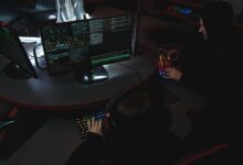 A group of people in a dark room working on computers, related to cybersecurity.