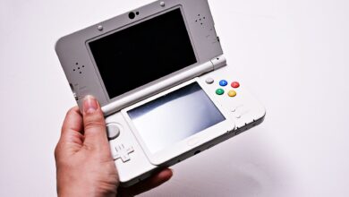 Close-up of a hand holding an open portable gaming console, featuring dual screens.