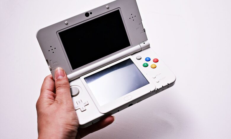 Close-up of a hand holding an open portable gaming console, featuring dual screens.