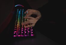 Close-up of hands typing on a colorful RGB backlit mechanical keyboard in a dimly lit environment.