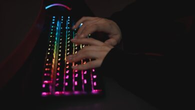 Close-up of hands typing on a colorful RGB backlit mechanical keyboard in a dimly lit environment.