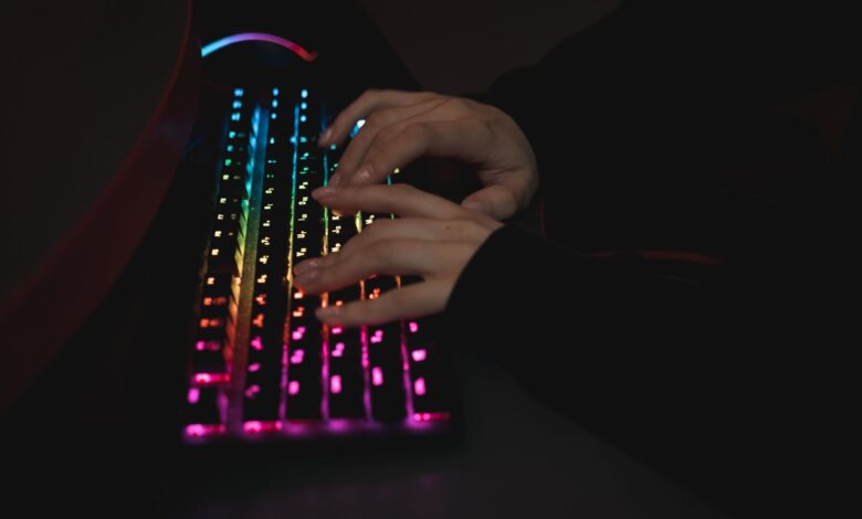 Close-up of hands typing on a colorful RGB backlit mechanical keyboard in a dimly lit environment.