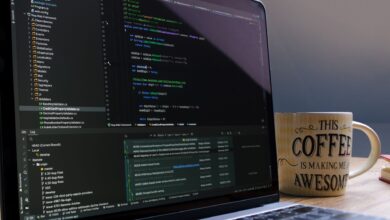 Close-up of laptop with coding software and a motivational coffee mug on a desk.
