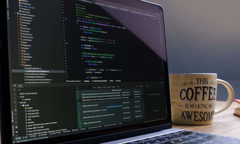 Close-up of laptop with coding software and a motivational coffee mug on a desk.