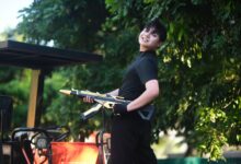 A cheerful teenager with a toy rifle poses outdoors in Vietnam under lush greenery.