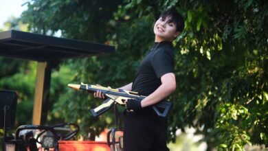 A cheerful teenager with a toy rifle poses outdoors in Vietnam under lush greenery.