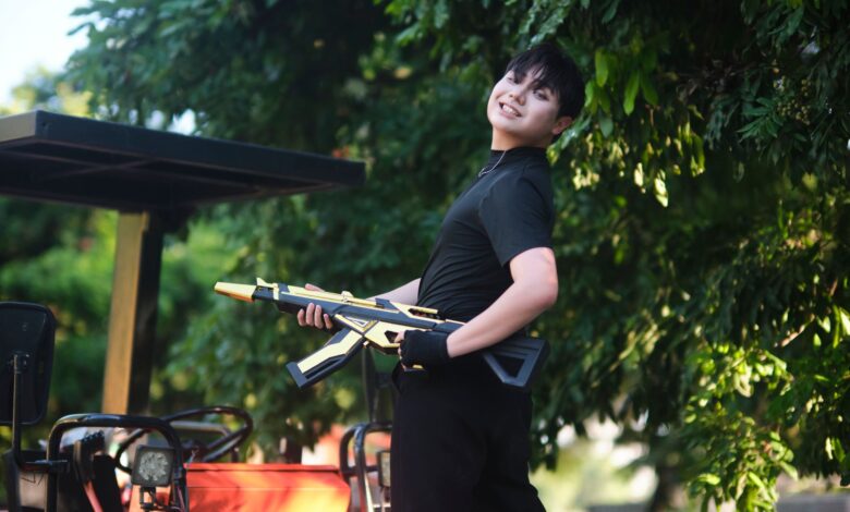 A cheerful teenager with a toy rifle poses outdoors in Vietnam under lush greenery.