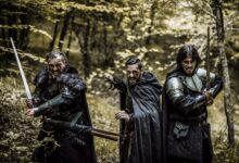 Three men in medieval armor and swords standing in a forest, ready for battle.
