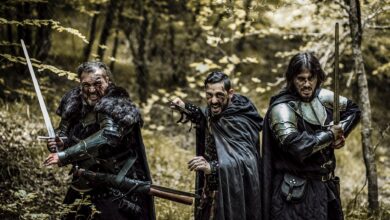 Three men in medieval armor and swords standing in a forest, ready for battle.