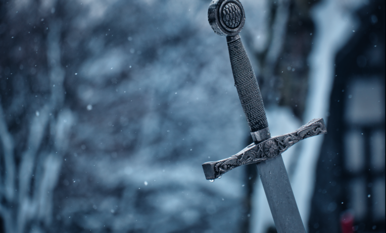 Close-up of a decorative medieval sword standing in a snowy outdoor setting.