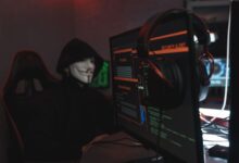 A person wearing a Guy Fawkes mask engaged in hacking activities on a computer in a dimly lit room.