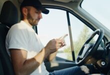 Side view of a man using a smartphone in a parked vehicle on a sunny day.