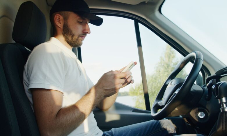 Side view of a man using a smartphone in a parked vehicle on a sunny day.