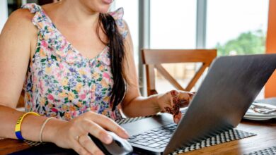 A woman using a laptop for remote work indoors, featuring a floral dress and henna design.