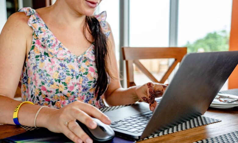 A woman using a laptop for remote work indoors, featuring a floral dress and henna design.