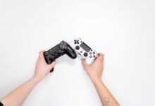 Top view of hands holding black and white game controllers on white background.