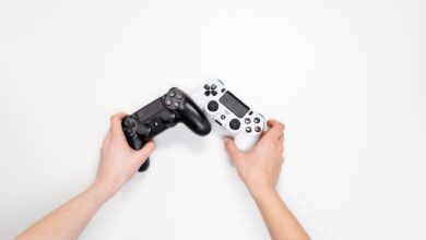 Top view of hands holding black and white game controllers on white background.
