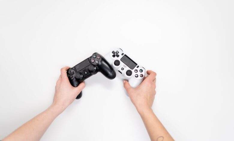 Top view of hands holding black and white game controllers on white background.