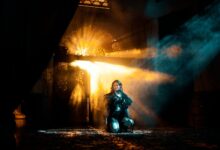 A young woman kneels in dramatic light and shadows, creating an ethereal atmosphere.