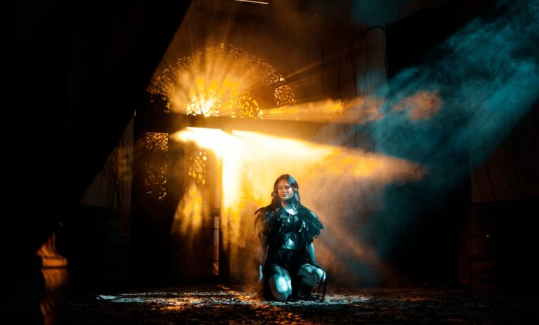 A young woman kneels in dramatic light and shadows, creating an ethereal atmosphere.