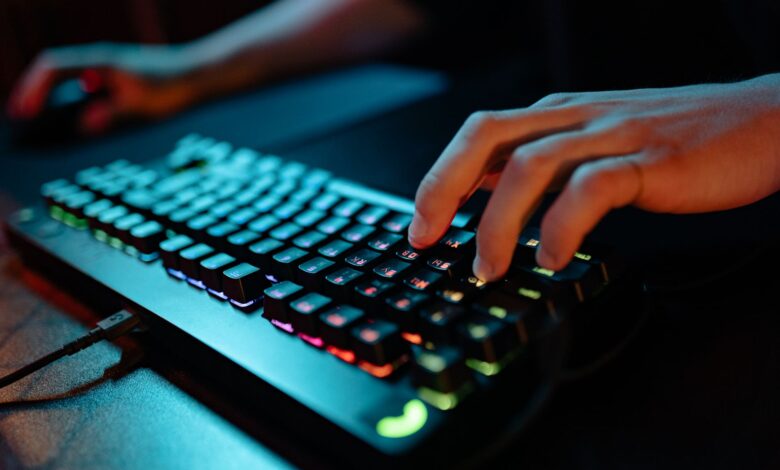 Hands typing on a glowing RGB keyboard during a gaming session indoors.