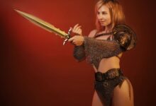 Woman in chainmail and armor holding a sword against a red background.