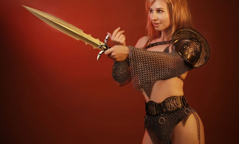 Woman in chainmail and armor holding a sword against a red background.