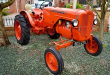 Bright orange Allis-Chalmers vintage tractor on display in a garden setting.