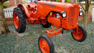 Bright orange Allis-Chalmers vintage tractor on display in a garden setting.