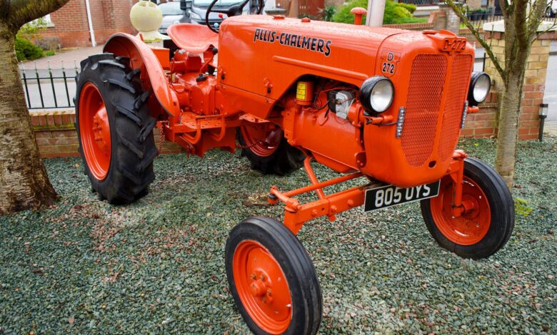 Bright orange Allis-Chalmers vintage tractor on display in a garden setting.