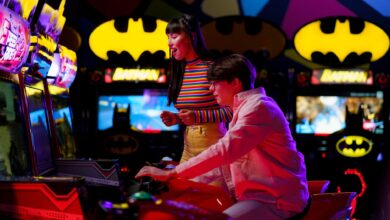 Couple enjoying an arcade gaming night surrounded by neon and Batman decor.