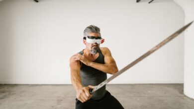 Adult man wearing VR headset practicing sword techniques in empty indoor space.