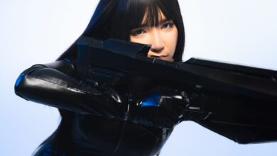 A person in sleek black cosplay attire holds a futuristic weapon, exuding a sci-fi vibe.