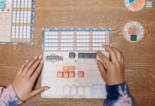 Hands arranging tiles on a strategic board game during a fun game night.
