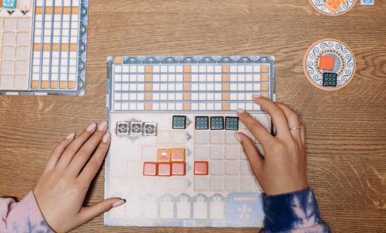 Hands arranging tiles on a strategic board game during a fun game night.