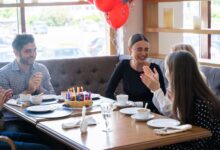 Friends celebrate a birthday with cake and laughter at a cozy restaurant setting.