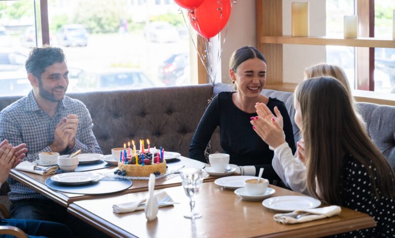 Friends celebrate a birthday with cake and laughter at a cozy restaurant setting.