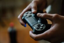 Crop anonymous male pressing buttons on console controller while playing video game in house on blurred background