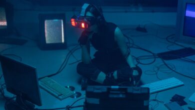 A woman in a dark room wearing a VR headset surrounded by retro technology.