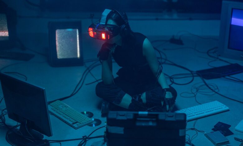 A woman in a dark room wearing a VR headset surrounded by retro technology.