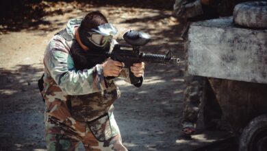 Man in camouflage gear aiming a paintball gun during an outdoor game.