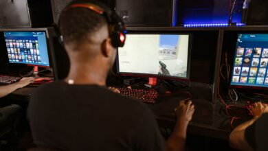 A man deeply engaged in a video game at a modern esports setup with multiple screens.